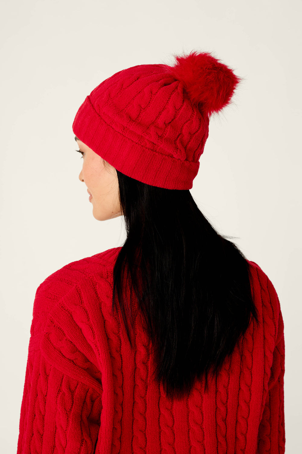Person wearing a Cozy Chenille Cable Knit Red Beanie With Pom-Pom and a matching red cable-knit sweater.