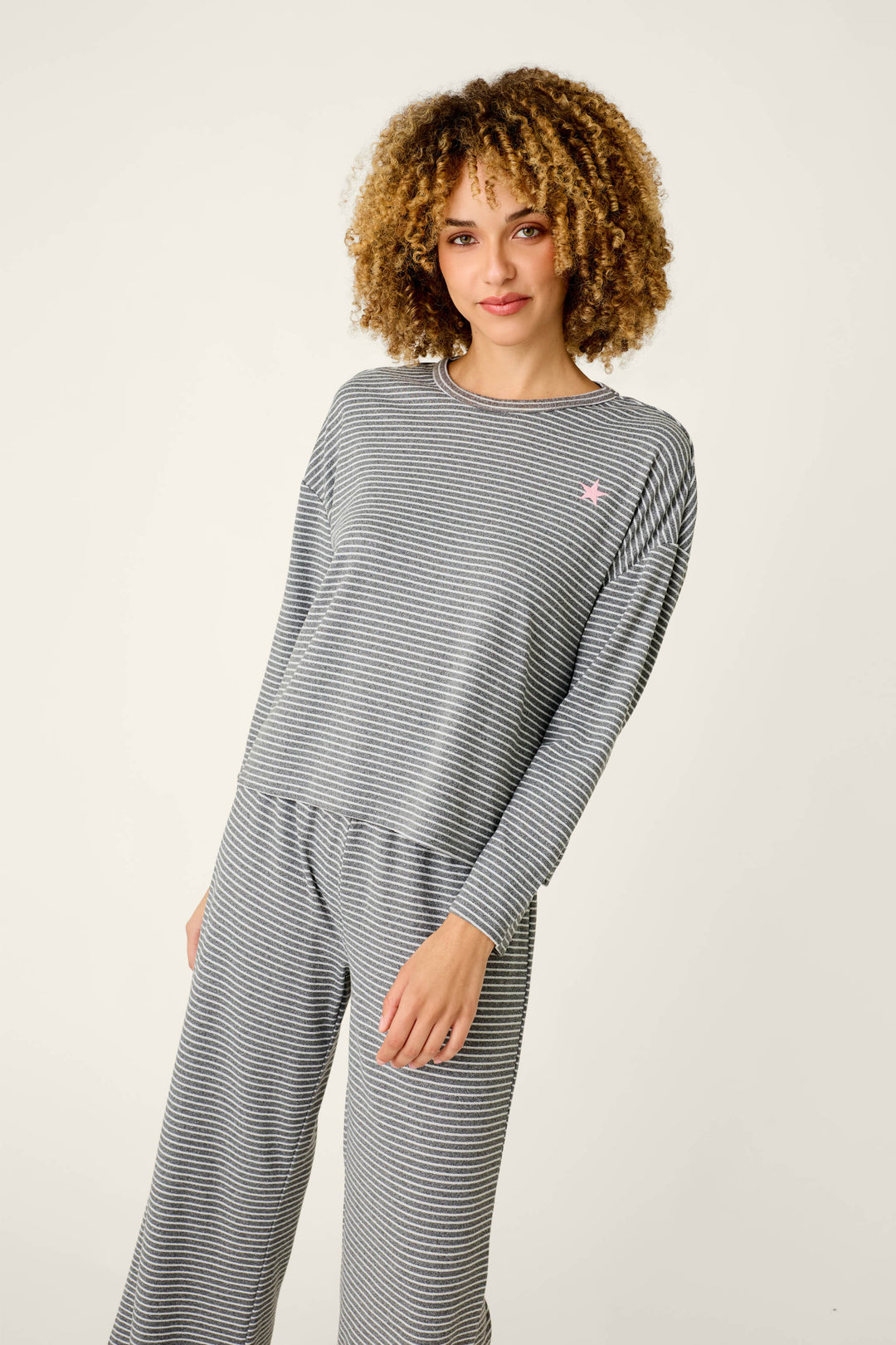 A woman wearing an Icon Stripes Heather Grey Long Sleeve PJ Set featuring grey and white stripes with a small pink star detail on the chest.