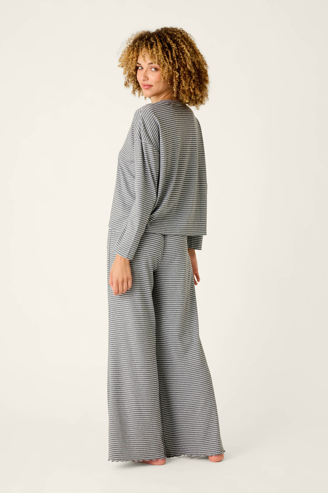 A woman wearing a P.J. Salvage Icon Stripes Heather Grey Long Sleeve PJ Set in a grey and white striped brushed pointelle fabric with a long-sleeve top and wide-leg pants.