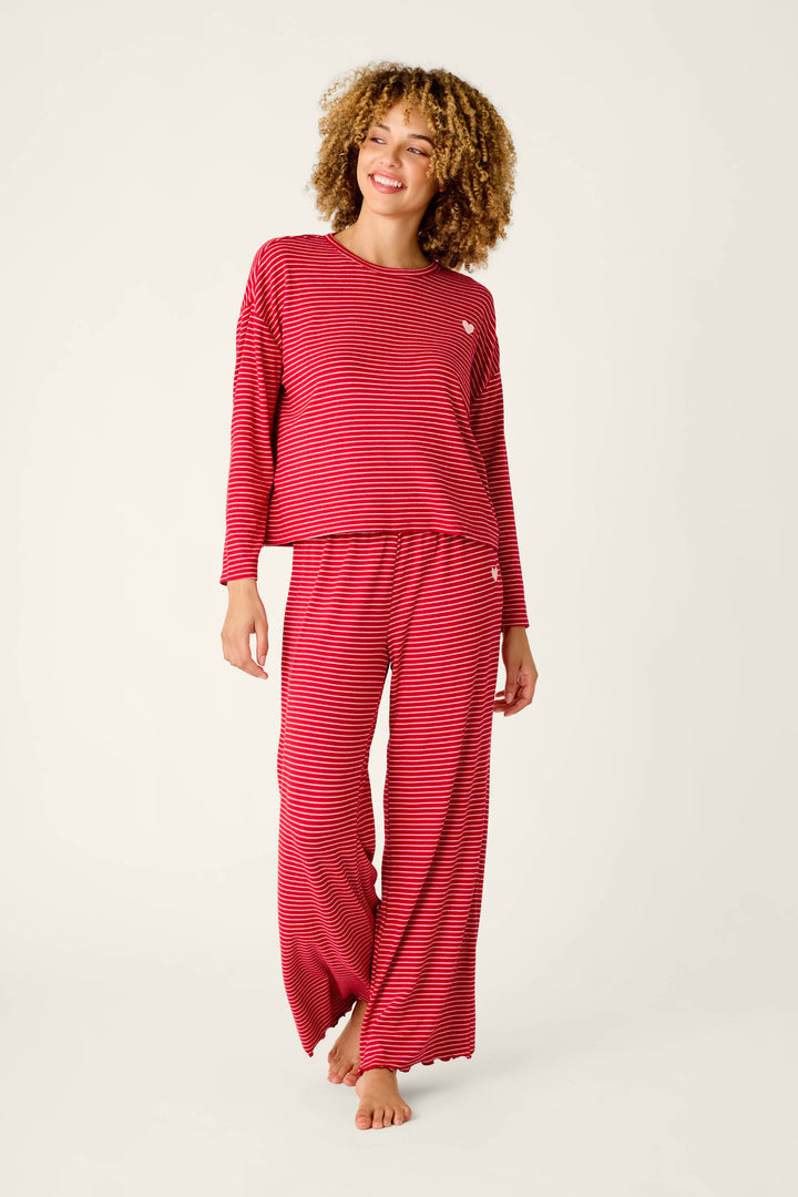 A person wearing an Icon Stripes Red Long Sleeve PJ Set, consisting of a red striped long-sleeved shirt and matching wide-leg pants.