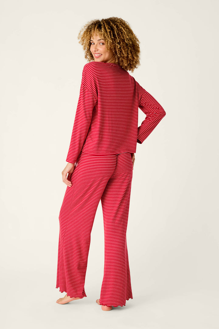 A woman with curly hair wearing an Icon Stripes Red Long Sleeve PJ Set, featuring a red and white fine horizontal stripe long-sleeved top and matching pants.