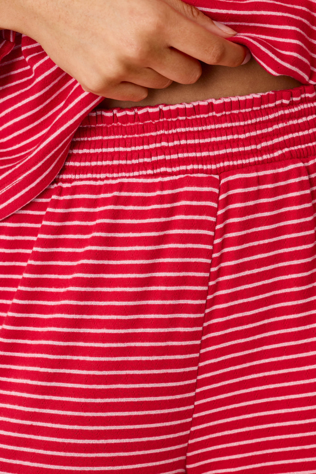 A person wearing an Icon Stripes Red Long Sleeve PJ Set, consisting of long-sleeved pajamas with thin white horizontal stripes and an elastic waistband.