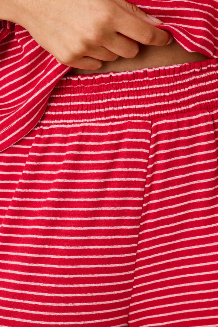 A person wearing an Icon Stripes Red Long Sleeve PJ Set, consisting of long-sleeved pajamas with thin white horizontal stripes and an elastic waistband.