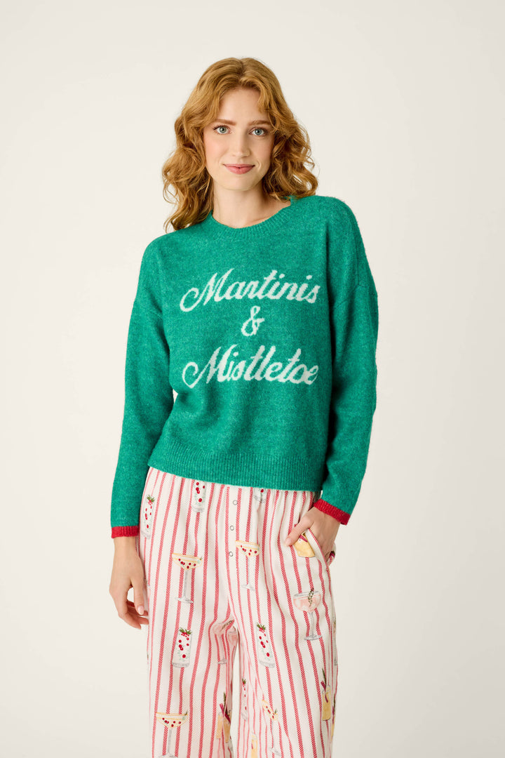 A person wearing a P.J. Salvage Martinis & Mistletoe Snuggle Sweater and white striped pajama pants with martini glass prints.
