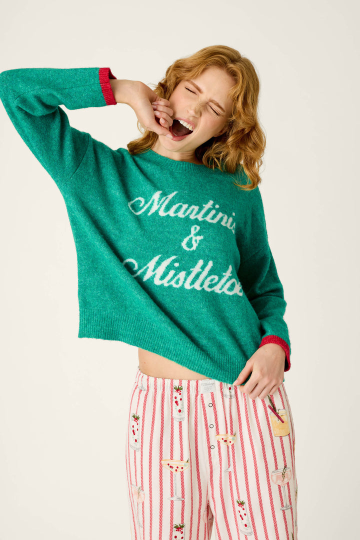 A woman yawning in a Martinis & Mistletoe Snuggle Sweater with Martini & Mistletoe in white script, paired with red-striped pajama pants featuring a martini print.