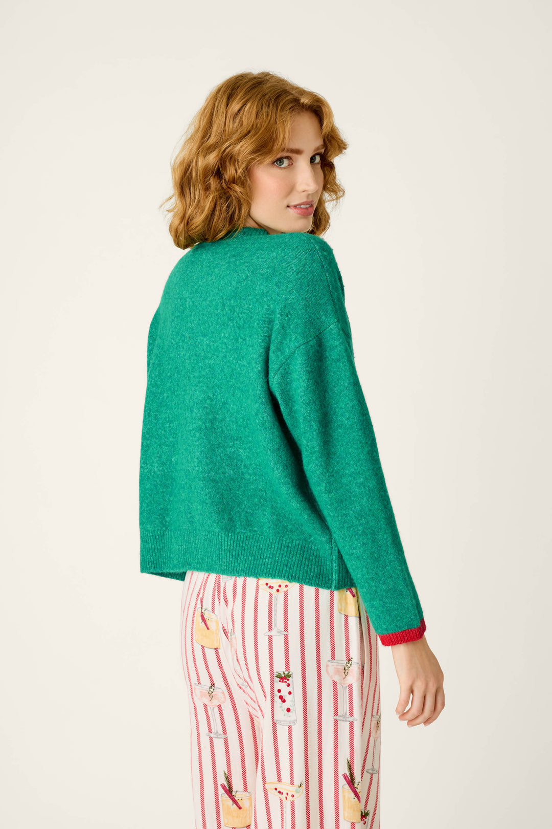 A person wearing a festive, green P.J. Salvage Martinis & Mistletoe Snuggle Sweater and white pants with a vertical red stripe and cocktail print.