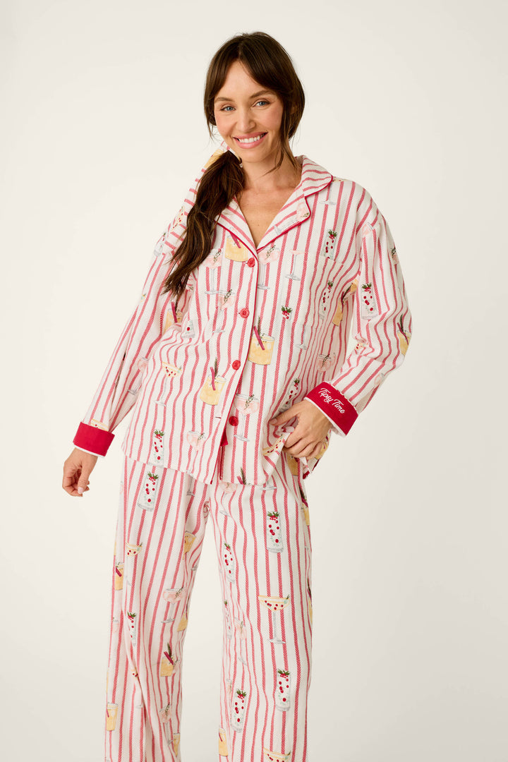 A woman wears a P.J. Salvage Martinis & Mistletoe Cocktail Print Flannel 3-Piece PJ Set, featuring a cozy white and red striped pattern with cocktail illustrations, red trim, and Tipsy Time embroidered on the sleeve cuff.