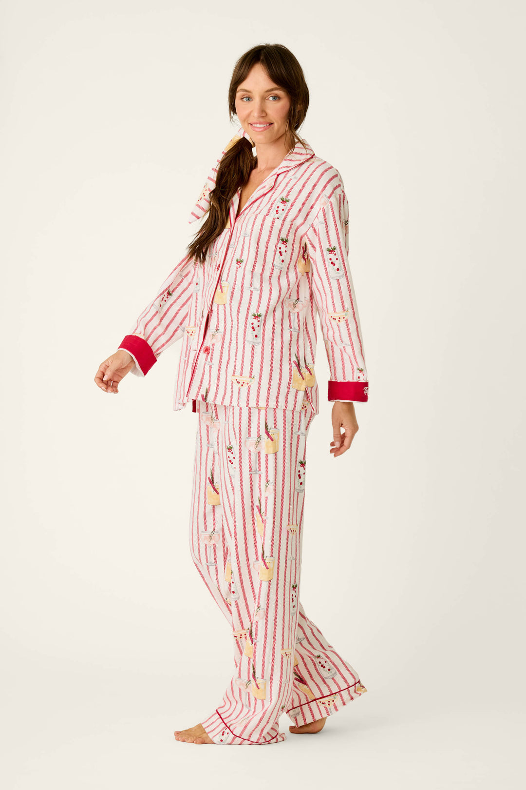 A woman wears a cozy P.J. Salvage Martinis & Mistletoe Cocktail Print Flannel 3-Piece PJ Set, consisting of a button-down top and matching trousers in a red-and-white striped pattern with a print of martini glasses garnished with mistletoe.