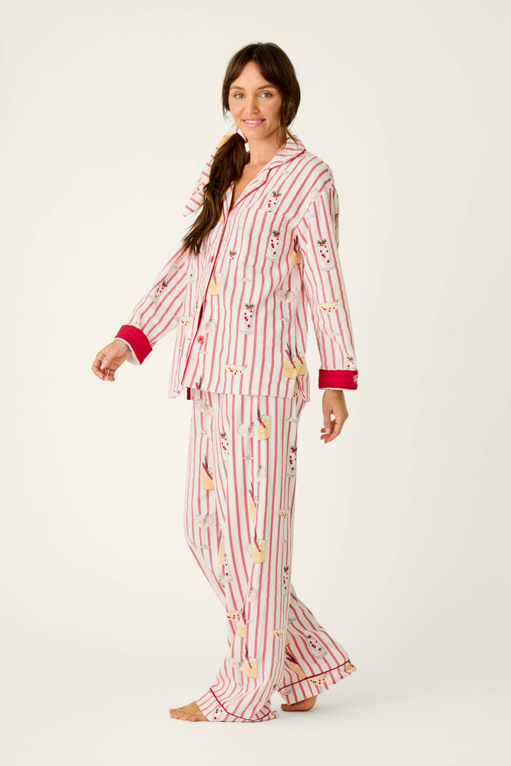 A woman wears a cozy P.J. Salvage Martinis & Mistletoe Cocktail Print Flannel 3-Piece PJ Set, consisting of a button-down top and matching trousers in a red-and-white striped pattern with a print of martini glasses garnished with mistletoe.