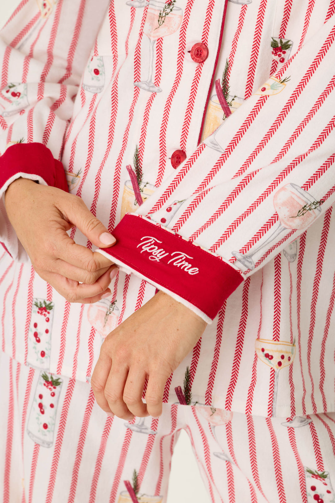 Person wearing a P.J. Salvage Martinis & Mistletoe Cocktail Print Flannel 3-Piece PJ Set featuring red herringbone stripes, a cocktail print, and Tipsy Time embroidered on the red sleeve cuff.