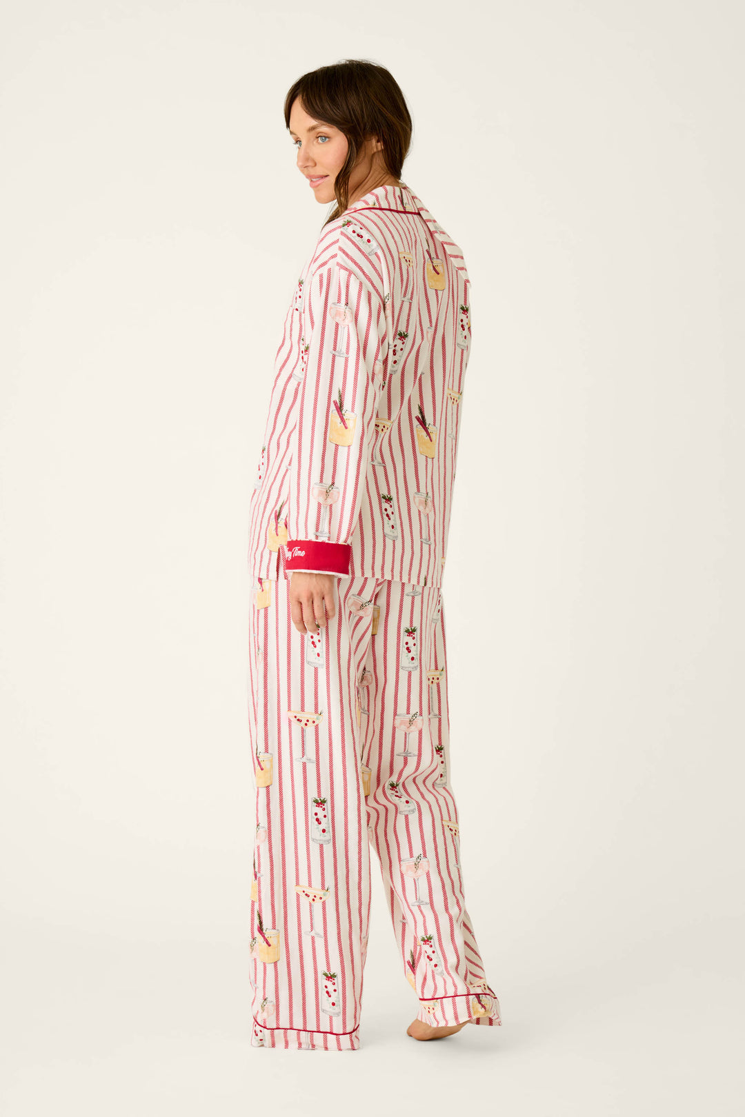 A person wearing a P.J. Salvage Martinis & Mistletoe Cocktail Print Flannel 3-Piece PJ Set, featuring a cozy long-sleeved button-up shirt and wide-leg pants with red vertical stripes and an all-over holiday cocktail print.