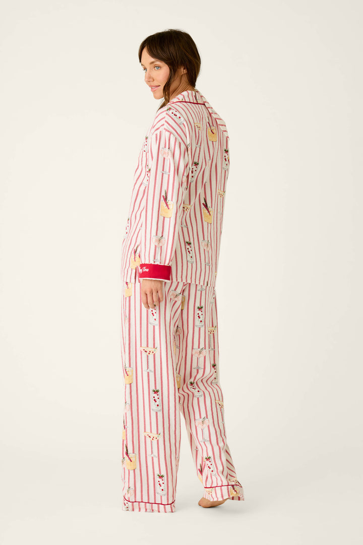 A person wearing a P.J. Salvage Martinis & Mistletoe Cocktail Print Flannel 3-Piece PJ Set, featuring a cozy long-sleeved button-up shirt and wide-leg pants with red vertical stripes and an all-over holiday cocktail print.