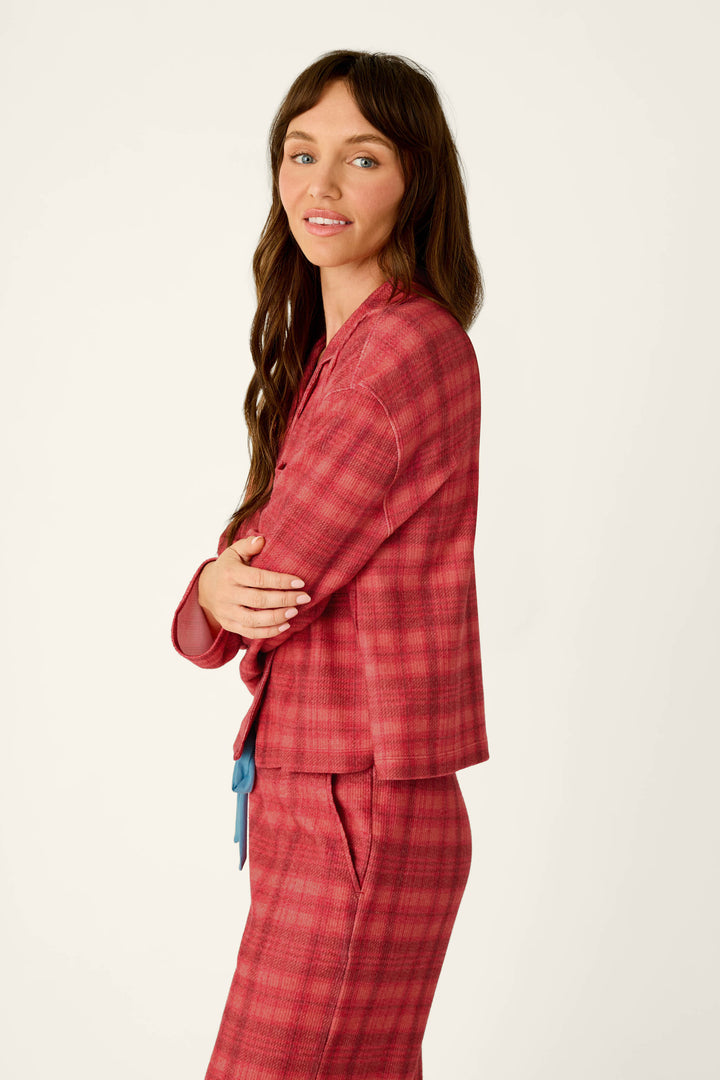 A woman with long wavy hair, shown from the side with her arms crossed, wearing a Mad for Plaid Long Sleeve Notch Collar Top and matching red plaid pants.