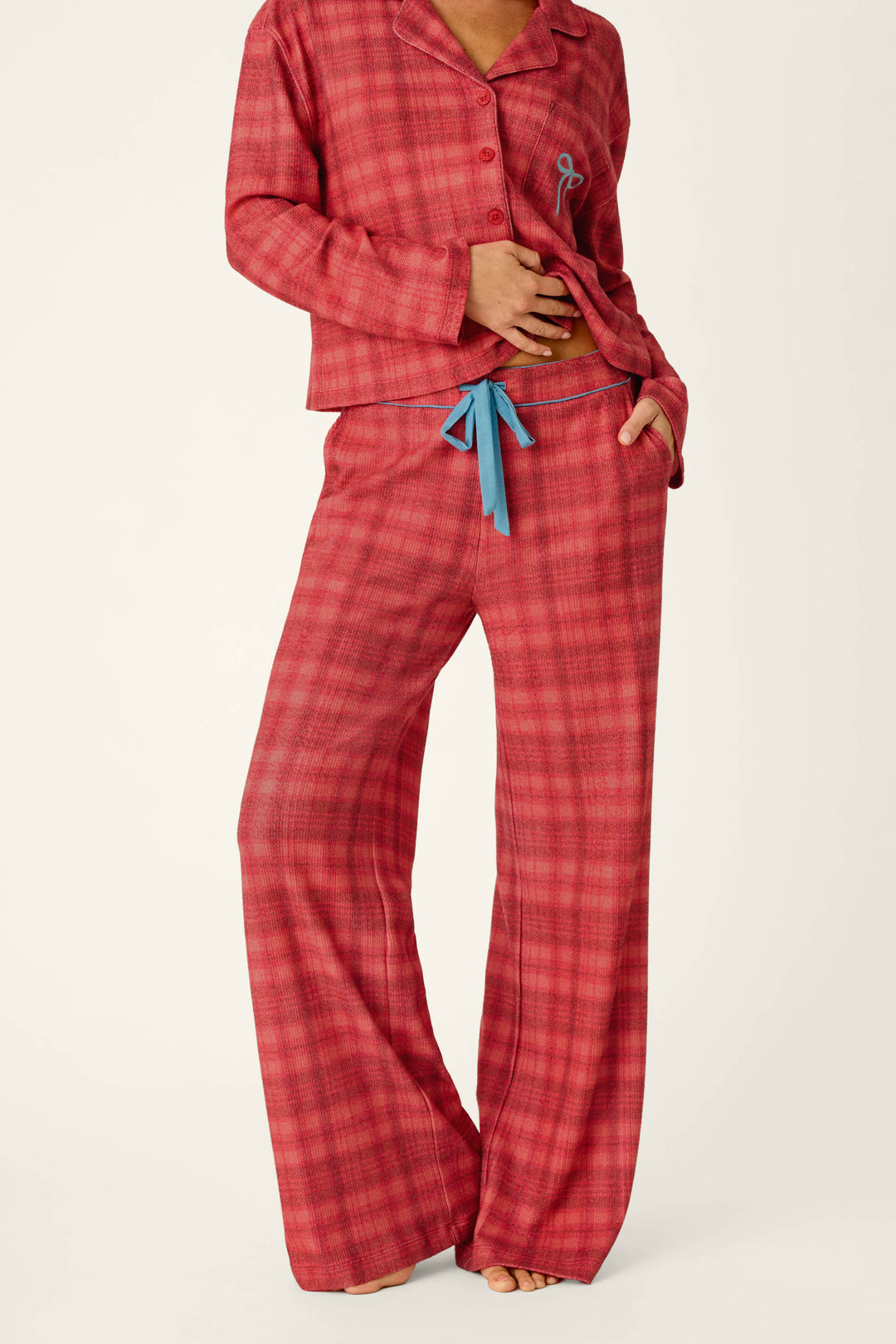 A person wearing cozy Mad for Plaid Pajama Pants, featuring a matching red plaid button-down top and wide-leg bottoms with a blue drawstring waist.