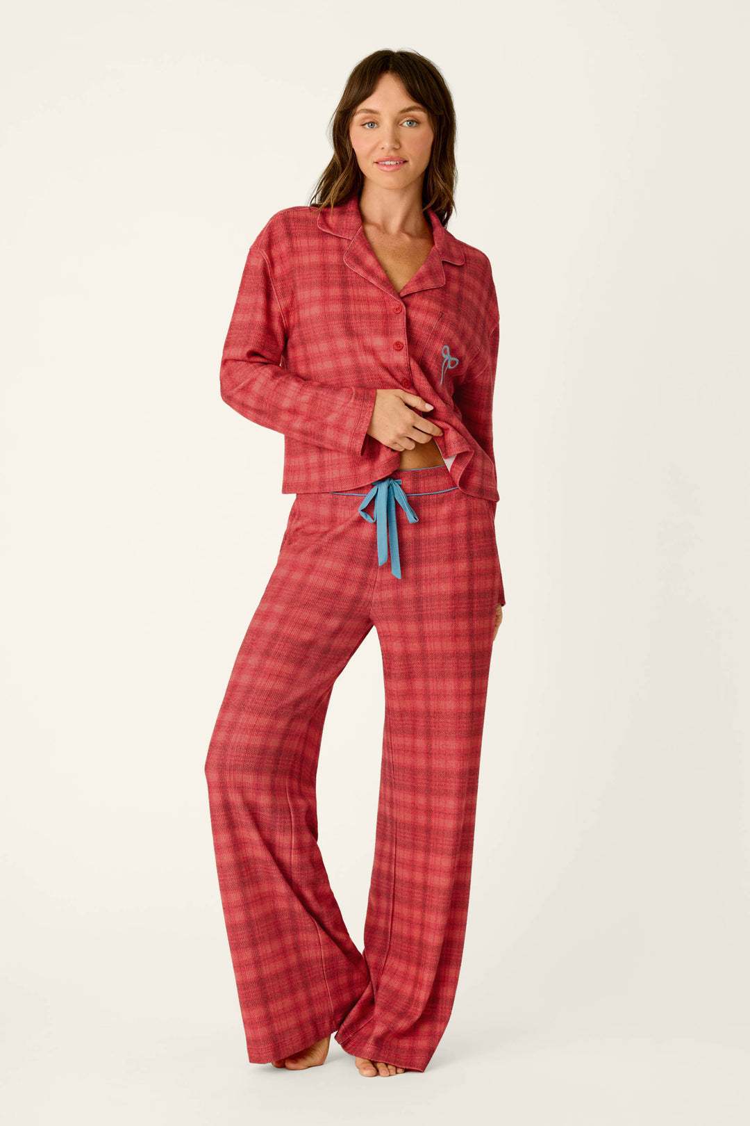 A person wearing long-sleeved holiday pajamas featuring Mad for Plaid Pajama Pants in a red plaid pattern with blue drawstring details.