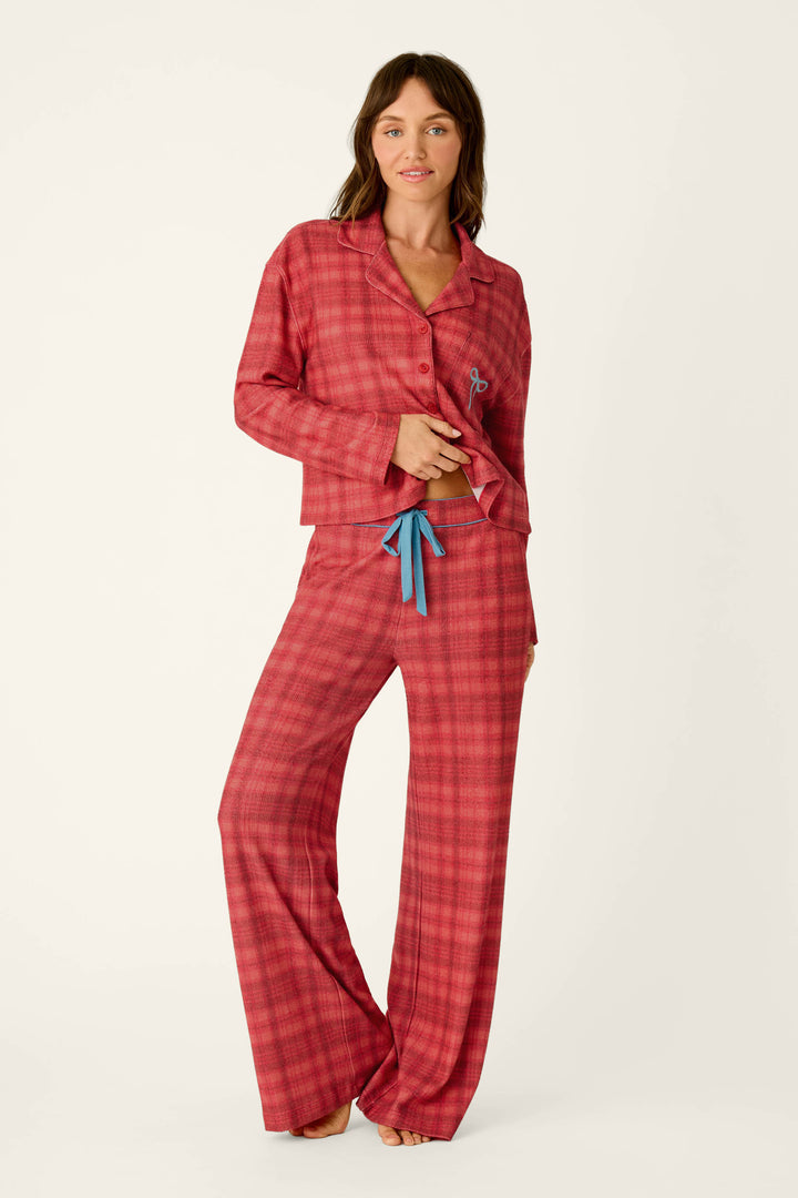 A person wearing long-sleeved holiday pajamas featuring Mad for Plaid Pajama Pants in a red plaid pattern with blue drawstring details.