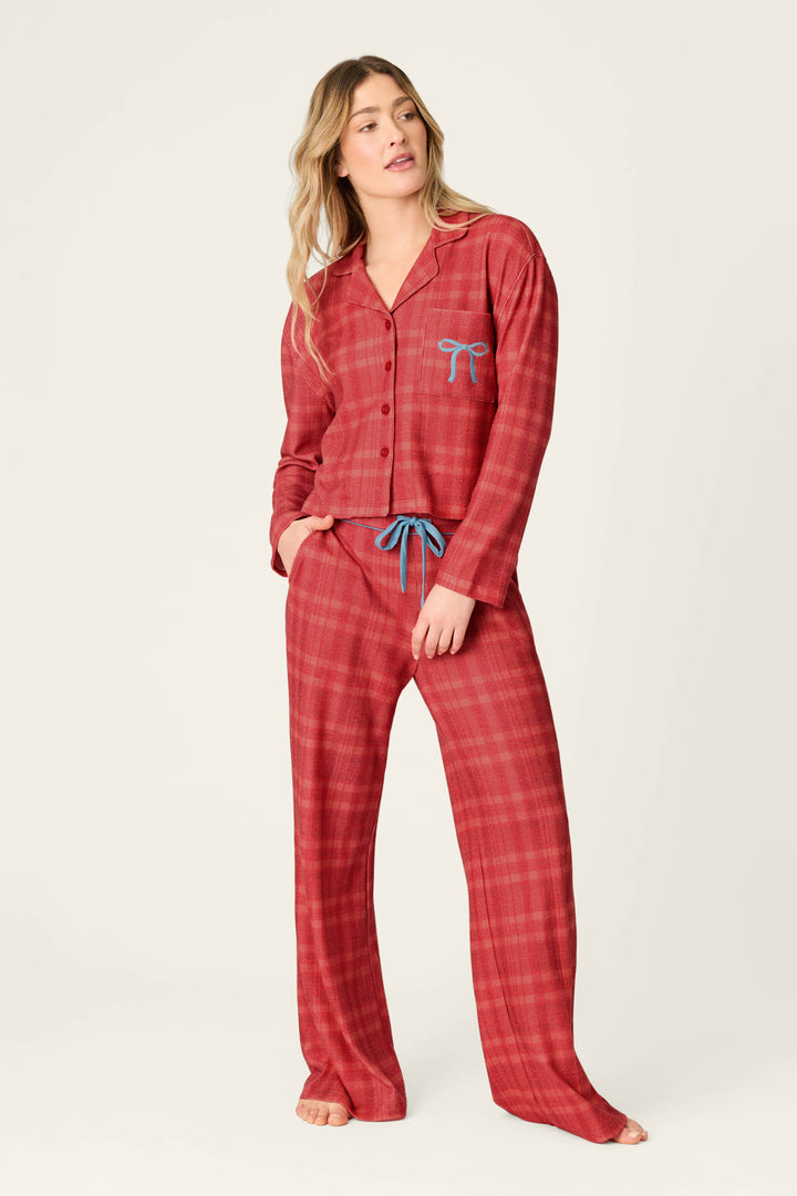A woman wearing a P.J. Salvage Mad for Plaid Long Sleeve & Pants PJ Set in red plaid with a blue bow detail on the pocket and a blue drawstring waist.