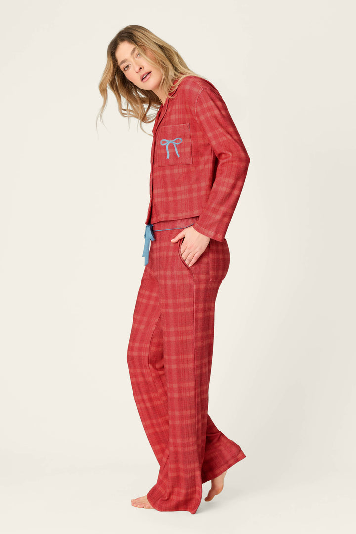 A person wears a P.J. Salvage Mad for Plaid Long Sleeve & Pants PJ Set, featuring a red plaid long-sleeve top with a light blue embroidered bow and matching wide-leg pants with a blue drawstring waist.