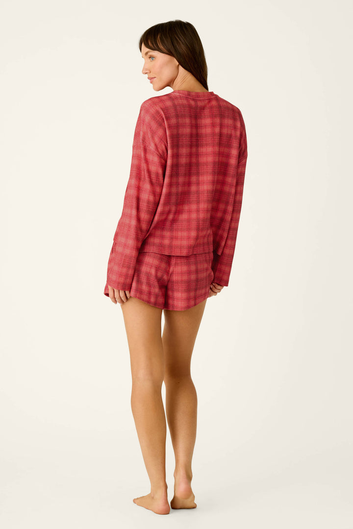 A woman wearing a red Mad for Plaid Long Sleeve & Shorts PJ Set, consisting of a cozy long-sleeve top and matching shorts.