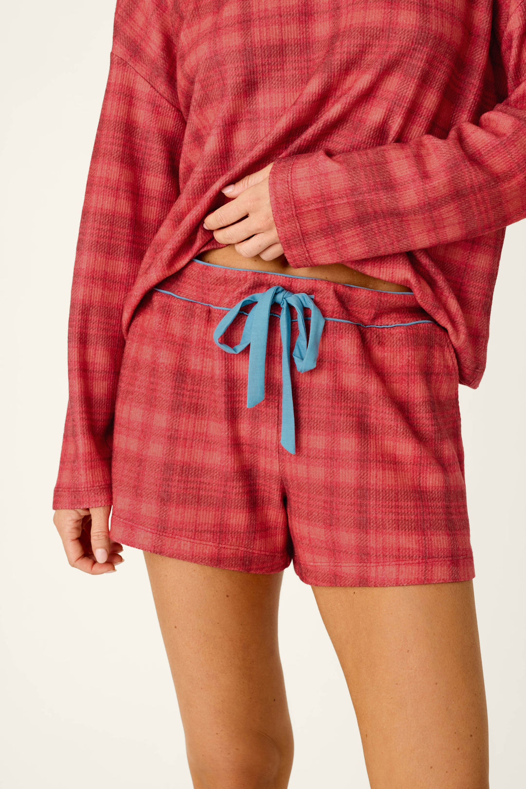 A person wearing red plaid Mad for Plaid Pajama Shorts with a blue drawstring waistband and a matching long-sleeved top.