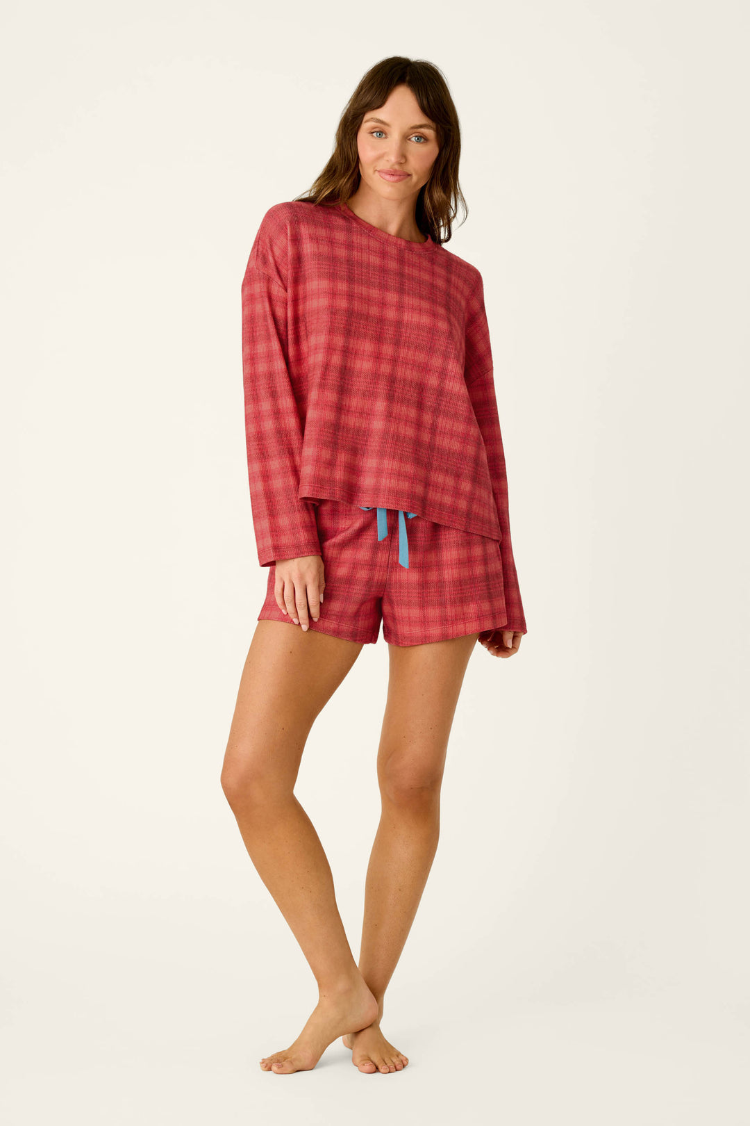A woman wearing a red plaid baby waffle knit long-sleeved top and matching Mad for Plaid Pajama Shorts with a blue drawstring.