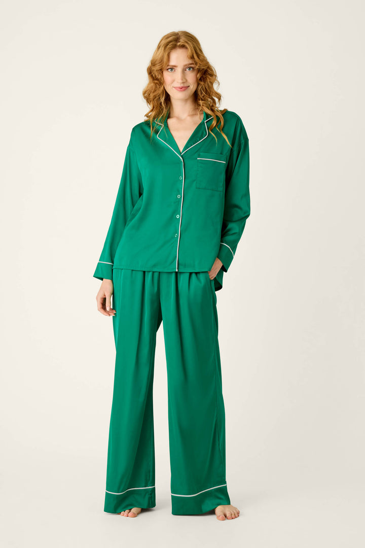 Woman wearing a P.J. Salvage Moonlight Muse Green Satin Long Sleeve PJ Set, featuring a luxe green satin long-sleeved shirt and matching wide-leg pants with white piping trim.