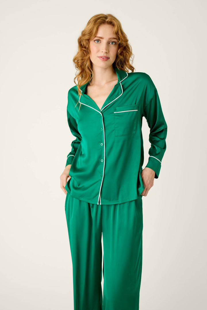 A woman wearing a P.J. Salvage Moonlight Muse Green Satin Long Sleeve PJ Set, featuring a luxe green satin long-sleeve, button-front top with white piping.