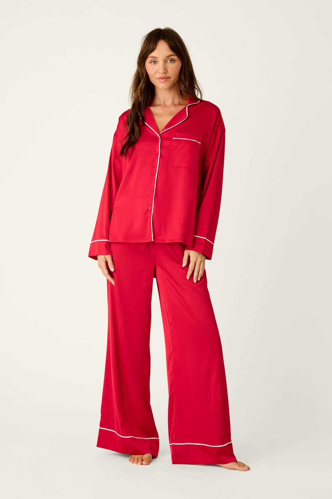A woman wearing a Moonlight Muse Red Satin Long Sleeve PJ Set, featuring a red satin pajama set with white piping on the collar, pocket, and pant cuffs.