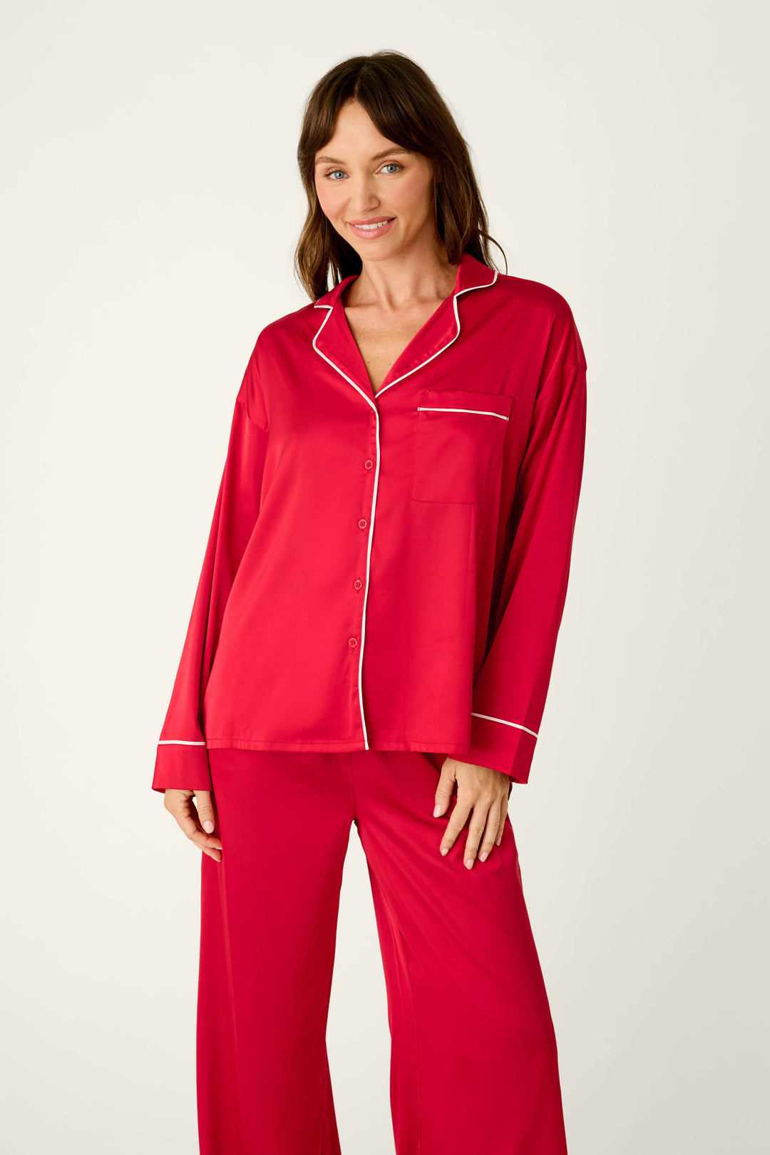 A woman wearing a Moonlight Muse Red Satin Long Sleeve PJ Set, featuring a red satin design with white piping on the collar, cuffs, and button placket.