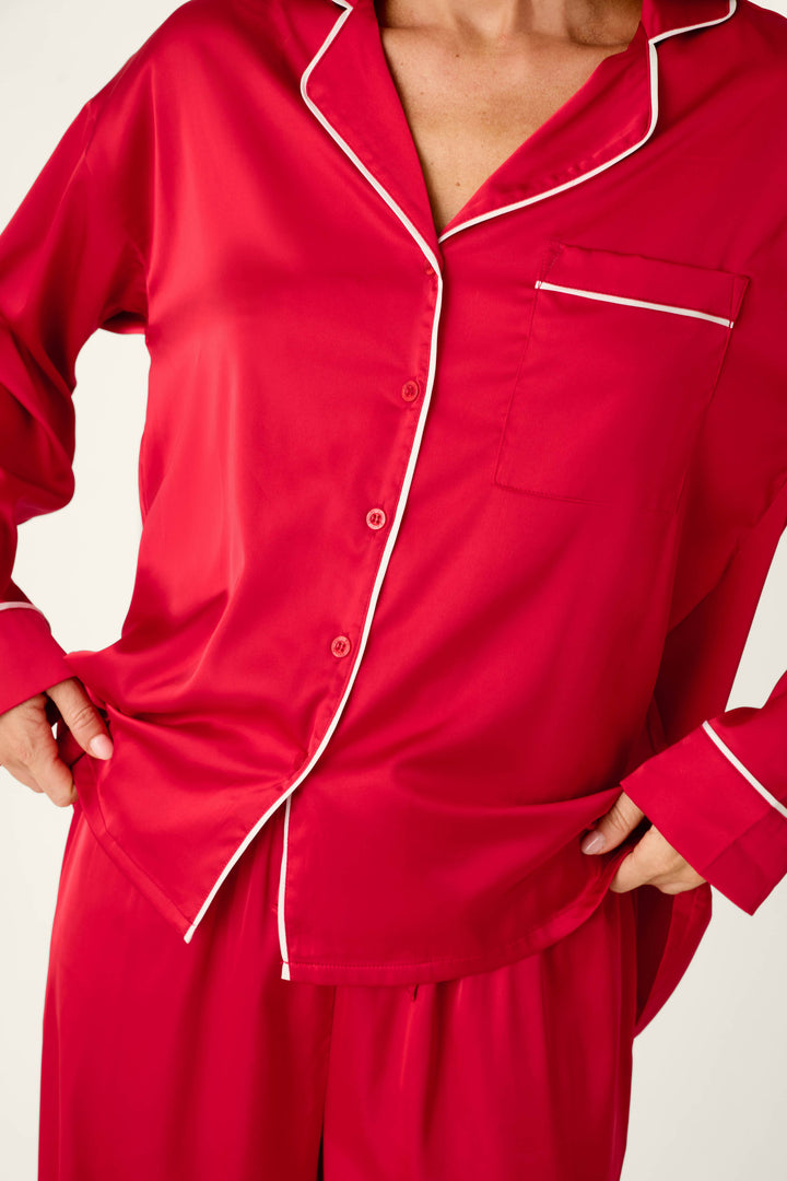 A person wearing a Moonlight Muse Red Satin Long Sleeve PJ Set, featuring a long-sleeved red luxe loungewear button-down pajama top with white piping detail.