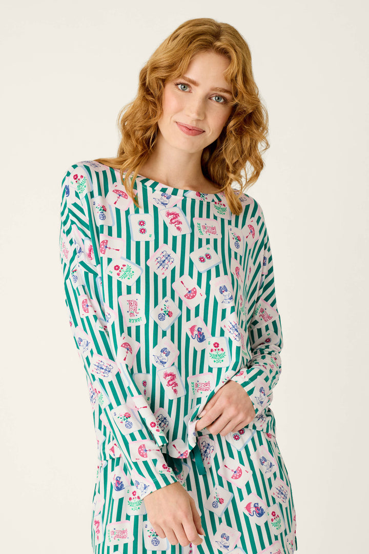 A person wearing a P.J. Salvage Mahjong Queen Dreams Long Sleeve Top, a modal jersey pajama shirt with a pattern of green vertical stripes and colorful tile illustrations.