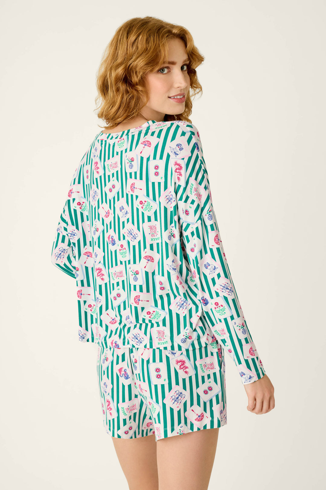 A woman seen from behind wearing the Mahjong Queen Dreams Long Sleeve Top and matching shorts, featuring a pattern of green vertical stripes and Mahjong tiles.