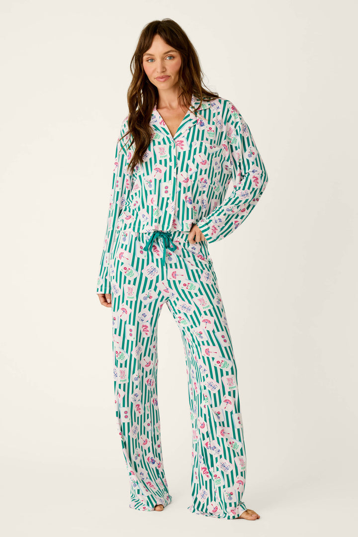 Woman wearing a long-sleeved button-down Mahjong Queen Dreams Pajama set made of modal jersey featuring a pattern of green vertical stripes and colorful mahjong tile illustrations.