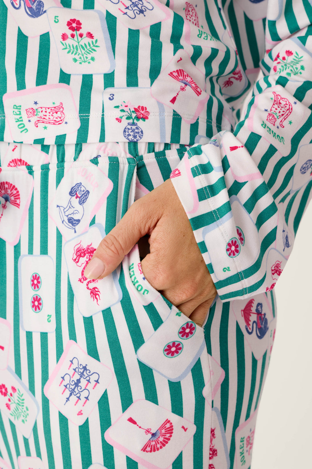 Green and white striped Mahjong Queen Dreams Pajama Pants by P.J. Salvage featuring colorful mahjong tile illustrations, shown with a hand tucked into a side pocket.