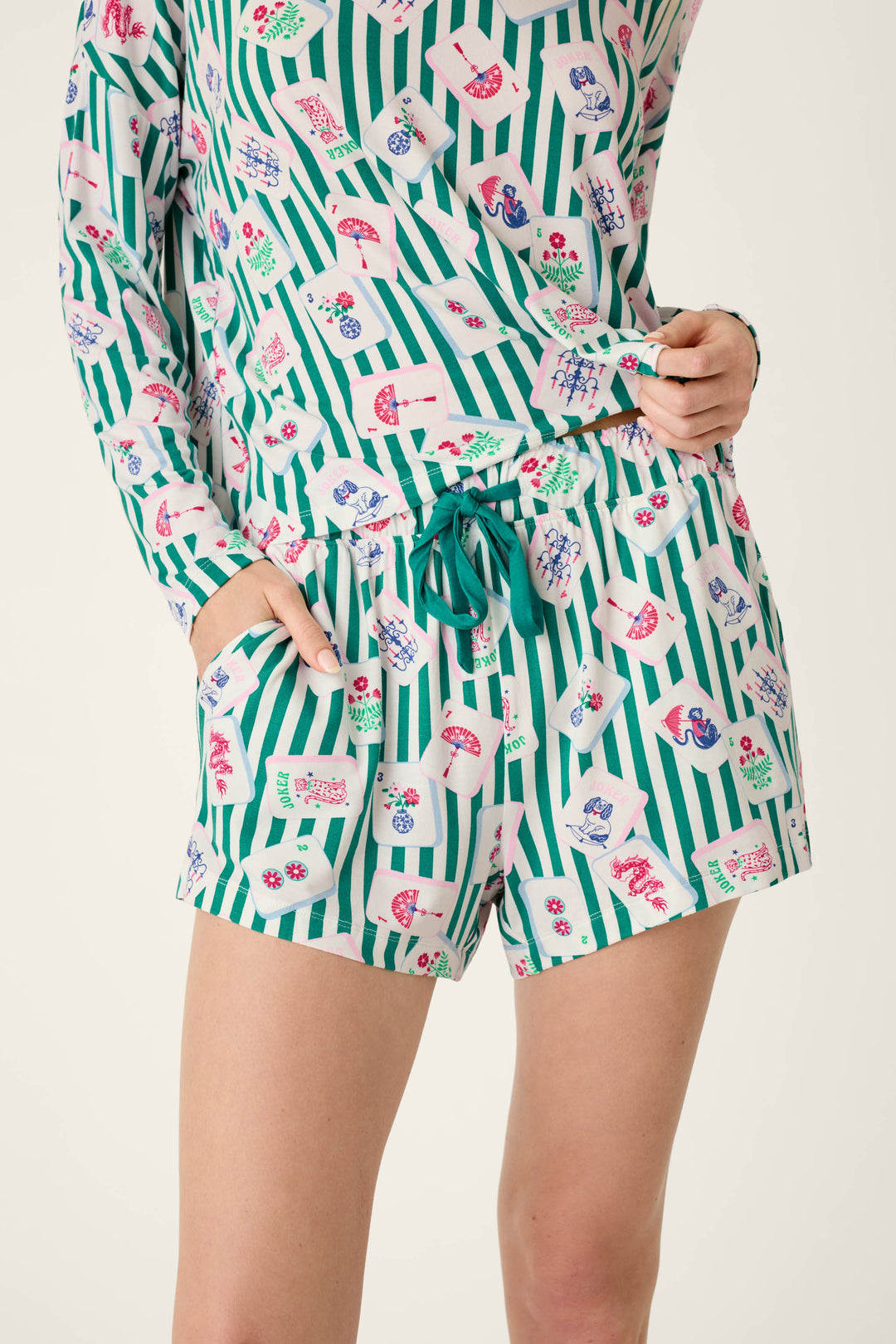 P.J. Salvage Mahjong Queen Dreams Pajama Shorts featuring a long-sleeved top and shorts in a green-and-white vertical stripe pattern with an all-over print of mahjong tiles and playing cards, finished with a green drawstring waist.