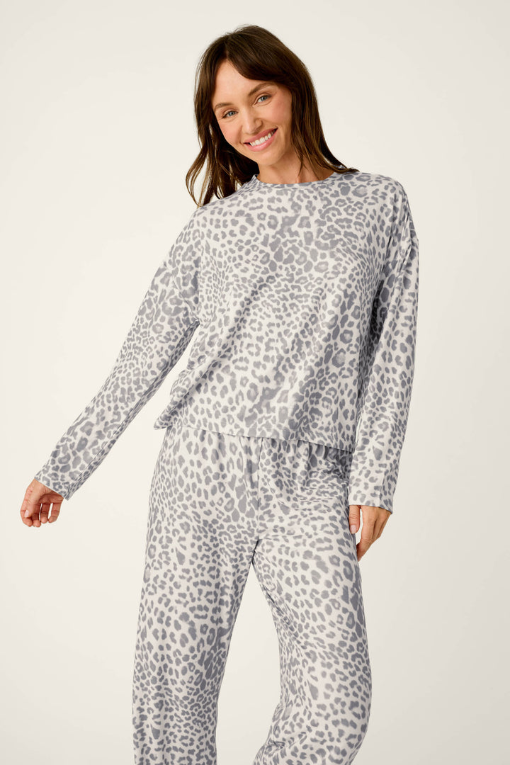 A smiling woman wears a cozy Wild About You Leopard Print Long Sleeve PJ Set, featuring a long-sleeved top and matching pants in a grey and white leopard print pattern.
