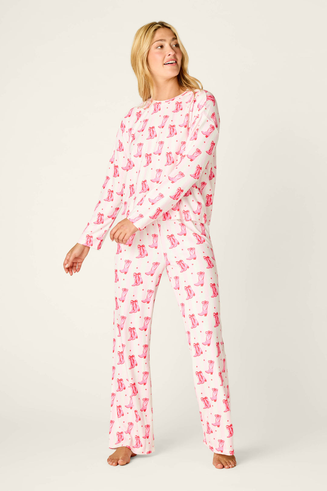 A woman wearing a Midnight Rodeo Cowboy Boots & Stripe Print Long Sleeve PJ Set, featuring a white background with an all-over print of pink cowboy boots and small red dots.