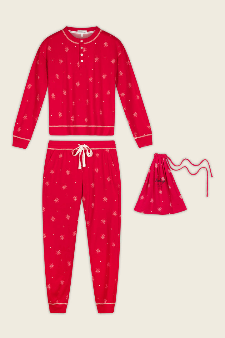 The P.J. Salvage Snowflakes Print 3-Piece PJ Gift Set, featuring a red long-sleeve top, drawstring pants with white snowflake patterns, and a matching drawstring bag, is displayed on a light background.