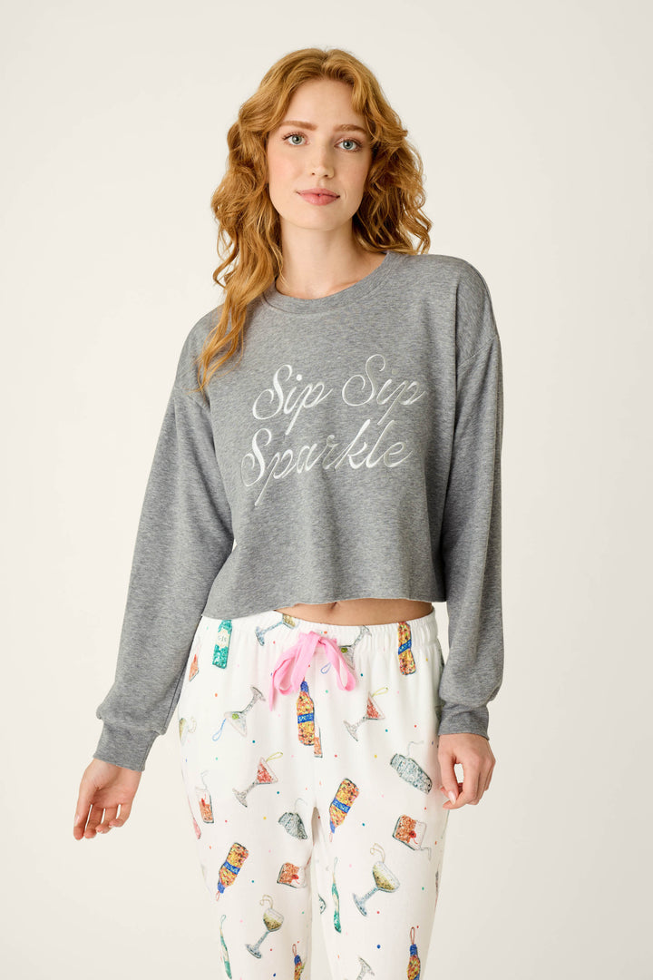 Woman wearing a Sip Sip Sparkle Sweatshirt and white patterned pajama pants with a pink drawstring.