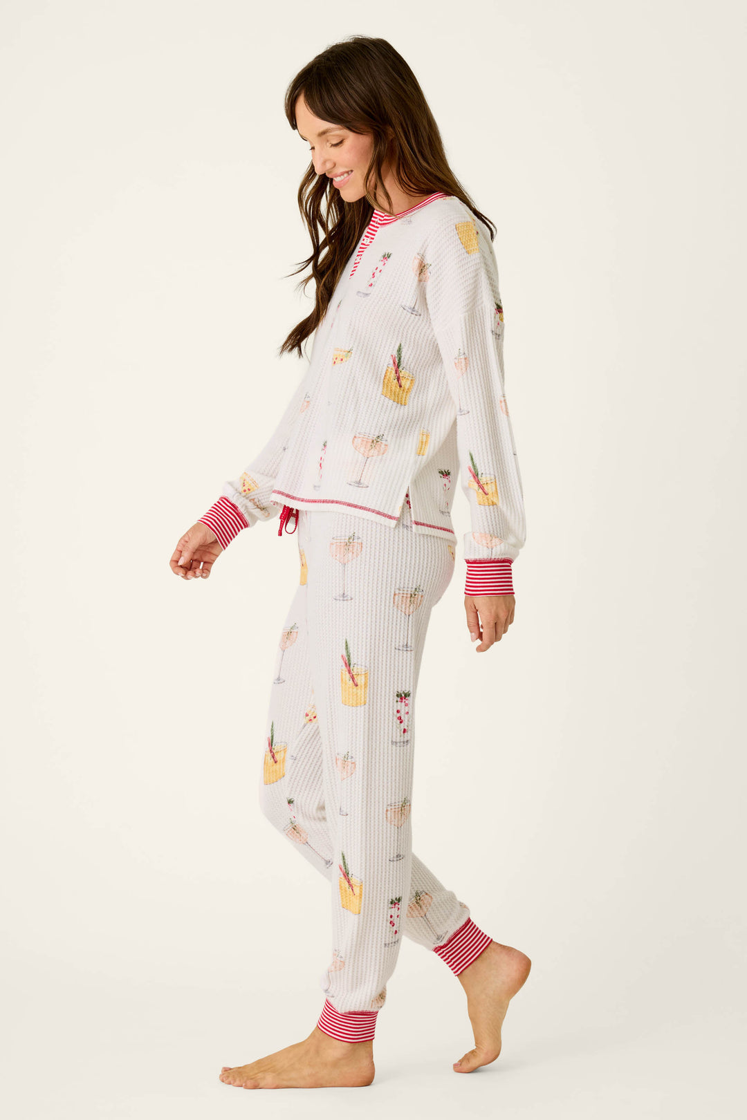 A woman wears a Ski Jammie Classics Cocktail Print Long Sleeve PJ Set in cozy brushed white fabric, featuring a pattern of colorful cocktails and red striped cuffs.