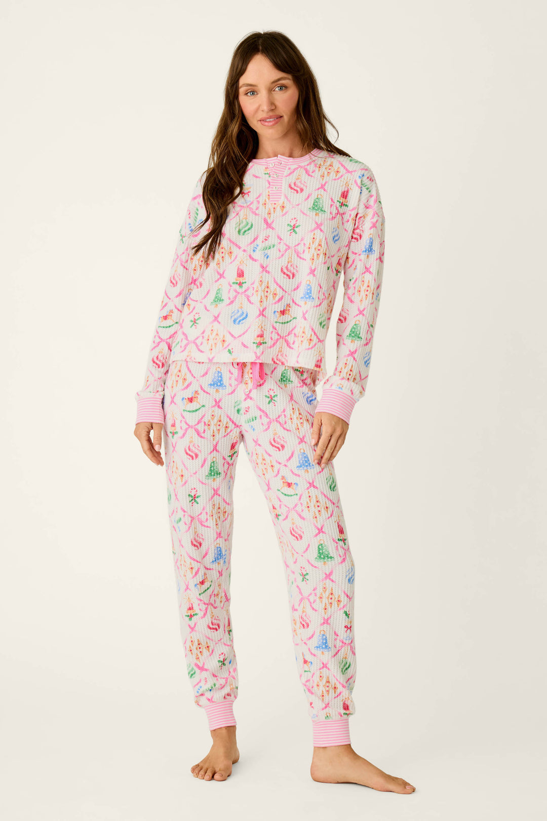 A woman models a P.J. Salvage Ski Jammie Classics Ornament Print Long Sleeve PJ Set, featuring a waffle-knit texture with Christmas ornaments and pink ribbons, finished with pink striped cuffs.