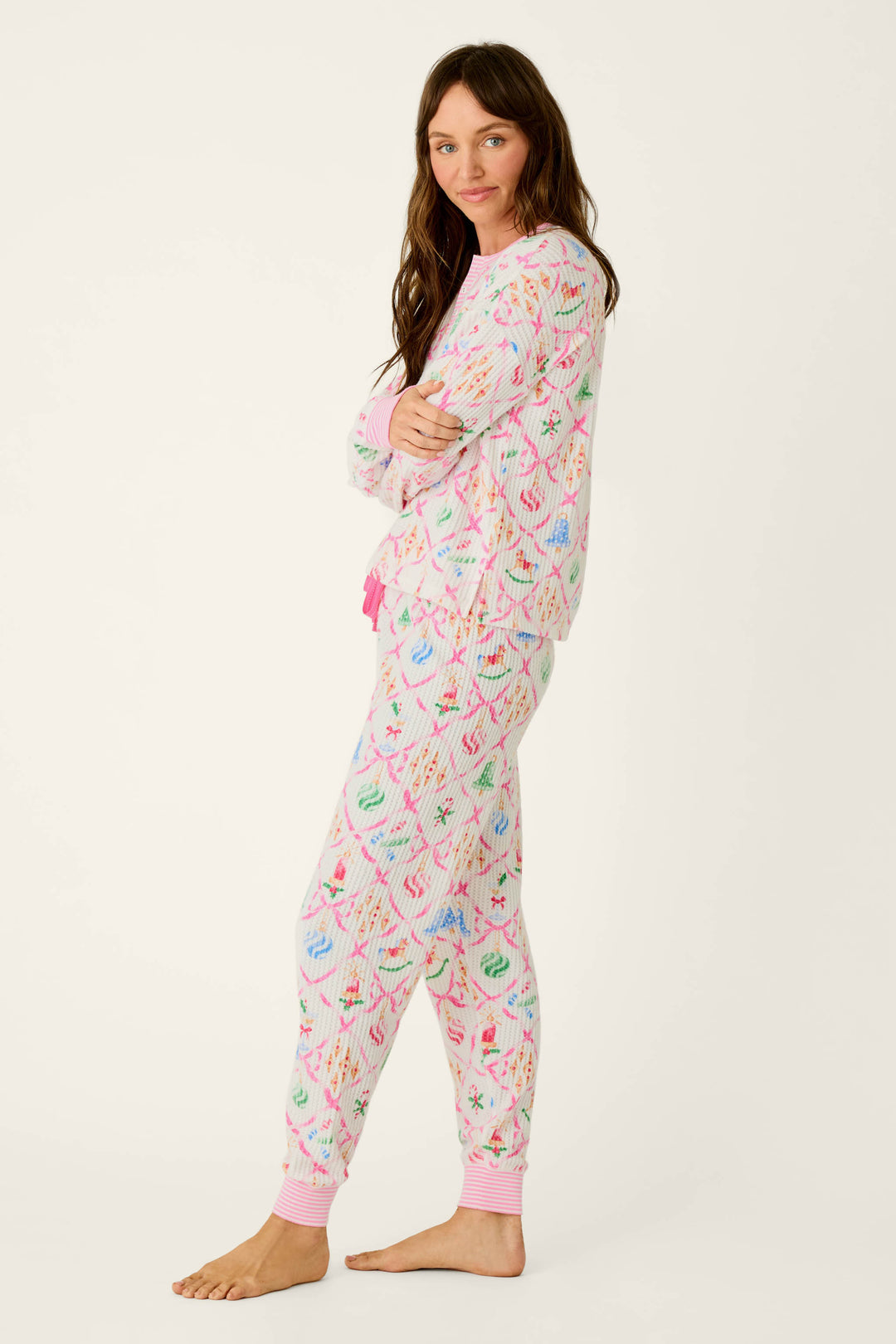 A woman in profile wears the P.J. Salvage Ski Jammie Classics Ornament Print Long Sleeve PJ Set, featuring a white waffle-knit fabric with a colorful holiday ornament pattern and pink striped trim.