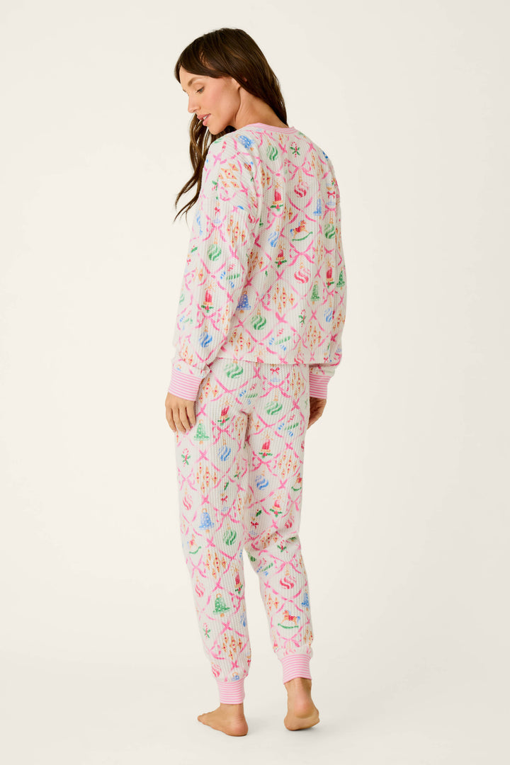 A woman wearing P.J. Salvage Ski Jammie Classics Ornament Print Long Sleeve PJ Set, featuring a white thermal texture with a repeating pattern of pink ribbons and colorful Christmas ornaments.