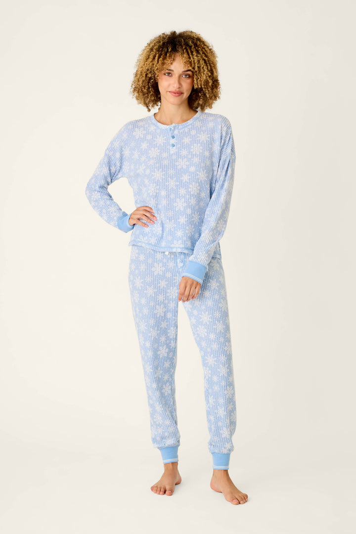 A woman wearing a light blue, long-sleeved Ski Jammie Classics Snowflake Print Long Sleeve PJ Set by P.J. Salvage with a white snowflake pattern.