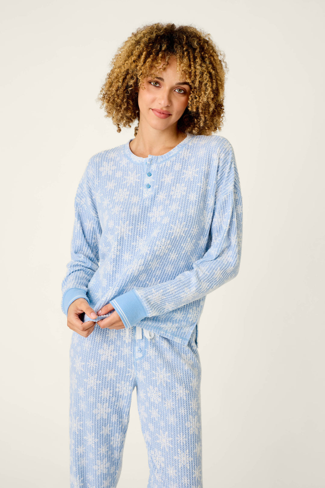 A woman wearing a light blue P.J. Salvage Ski Jammie Classics Snowflake Print Long Sleeve PJ Set, featuring a cozy thermal long-sleeved top and matching pants with a white snowflake pattern.
