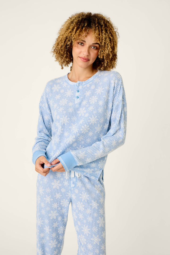 A woman wearing a light blue P.J. Salvage Ski Jammie Classics Snowflake Print Long Sleeve PJ Set, featuring a cozy thermal long-sleeved top and matching pants with a white snowflake pattern.