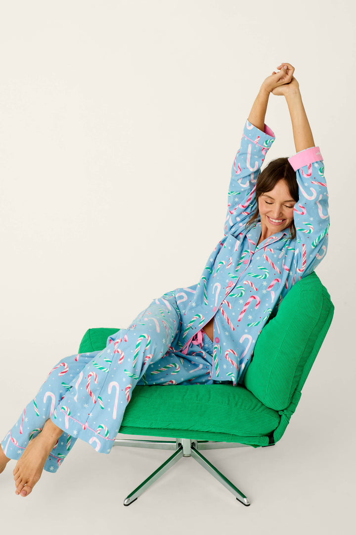 A woman in The Sweetest Season Candy Cane Print Flannel 3-Piece PJ Set stretches while sitting in a green corduroy chair.