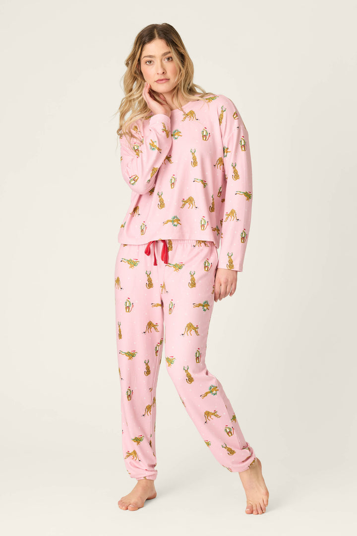 A person wearing a pink Very Merry Wild for the Holidays Long Sleeve Top and matching joggers, featuring a repeating print of leopards wearing Santa hats and holiday wreaths.