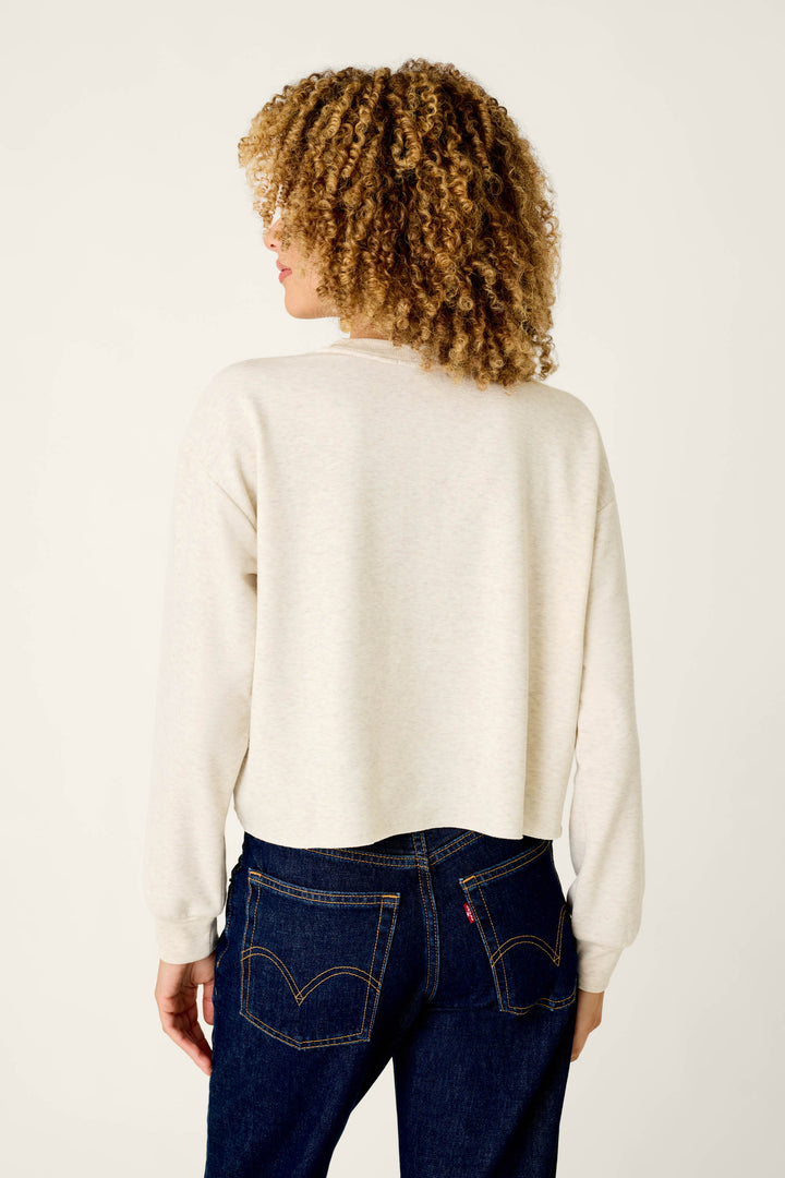 A person viewed from the back, wearing a cream-colored Very Merry Bouclé Merry Sweatshirt with Merry embroidery and dark blue jeans.