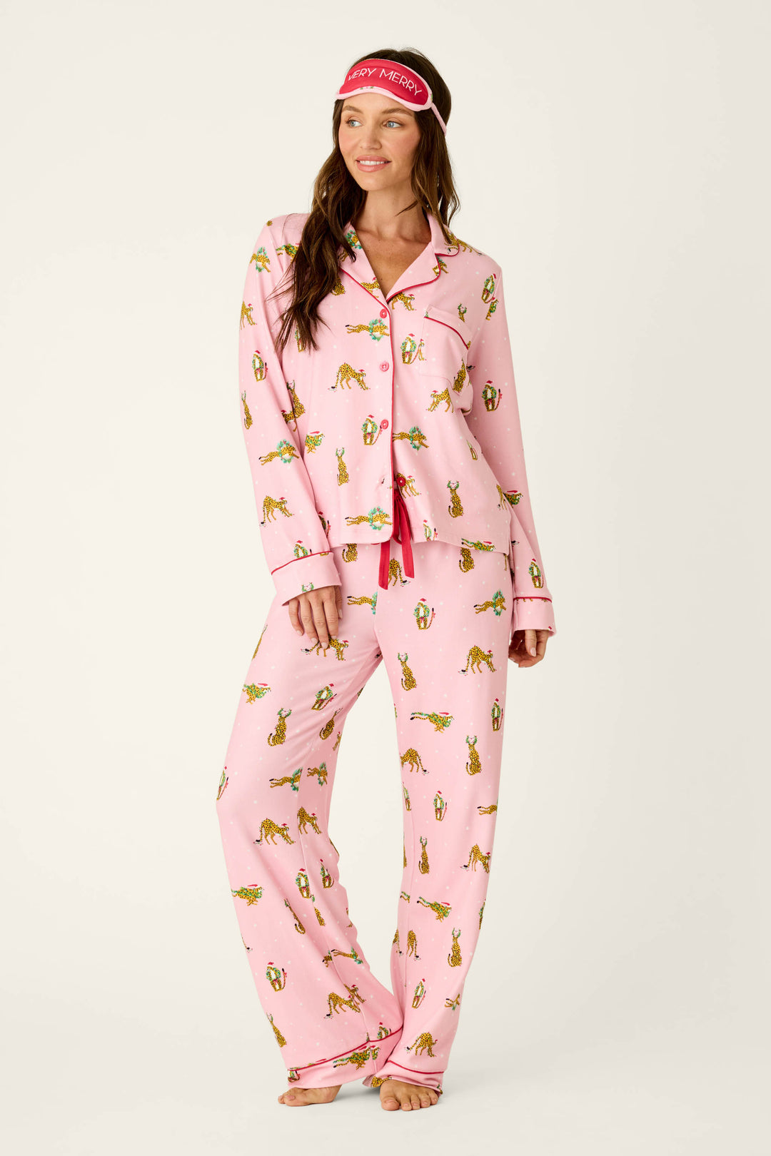 A woman wears a P.J. Salvage Very Merry Wild for the Holidays 3-Piece PJ Set featuring leopard print and animals in Santa hats, paired with a matching sleep mask on her forehead.